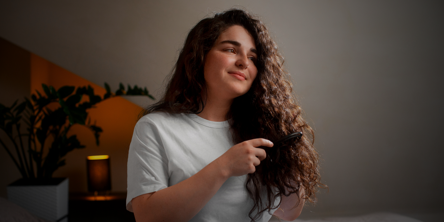 Woman with curly hair holding a hairbrush in a dimly lit room.